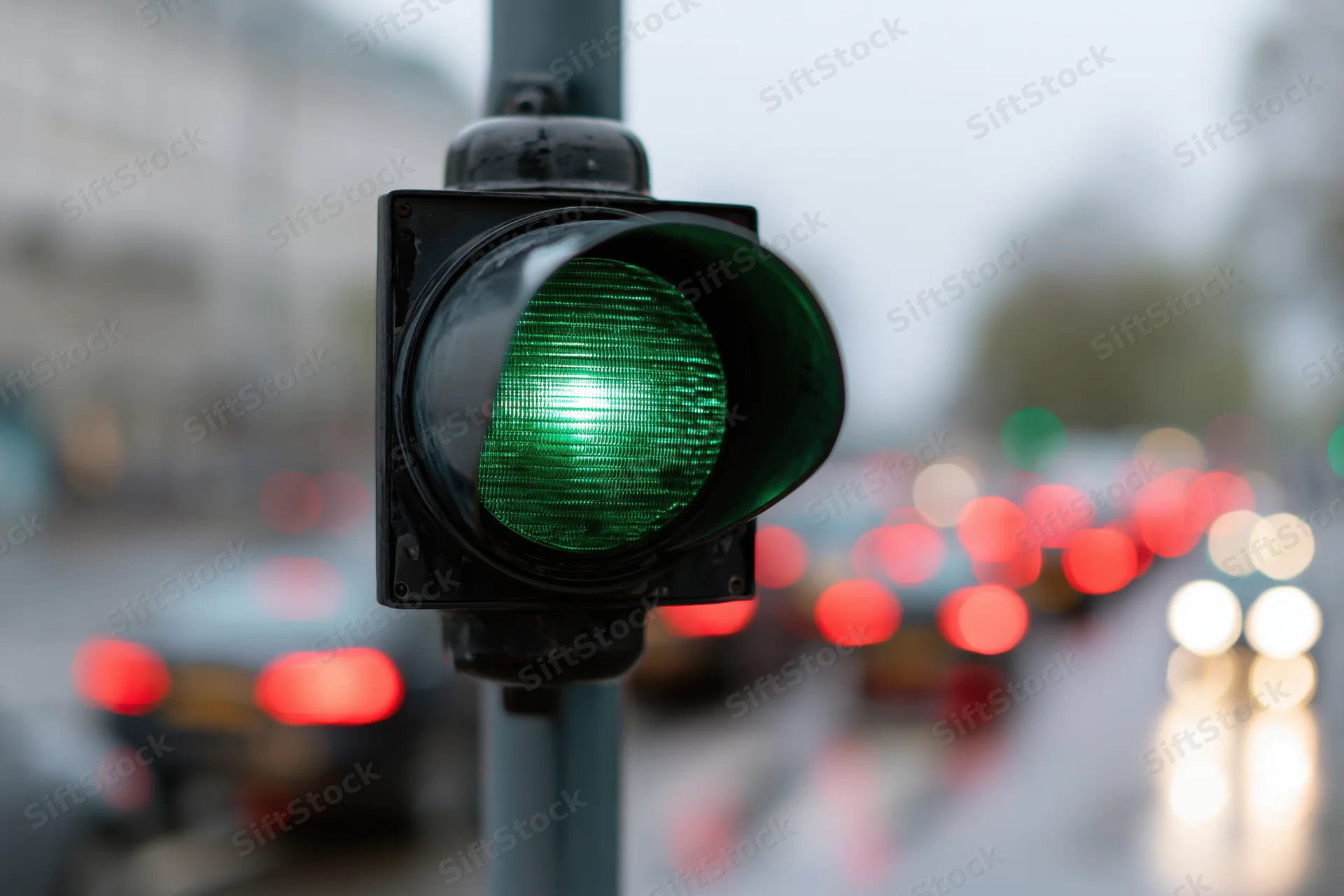 Green traffic light illuminated on a wet city street with blurred vehicles and taillights in the background
