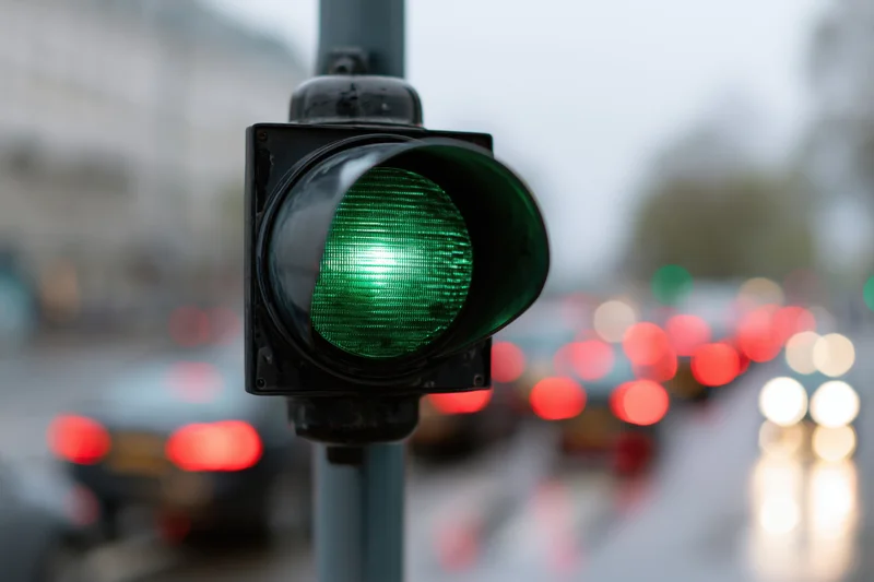 Green traffic light illuminated on a wet city street with blurred vehicles and taillights in the background