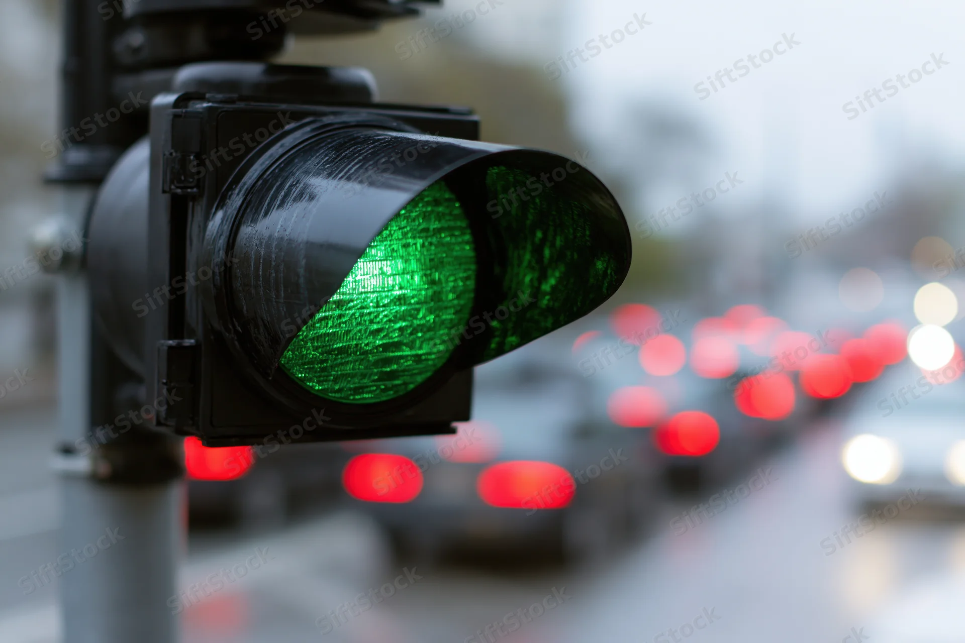 Close-up of a green traffic light signal on a city street with blurred vehicles in the background