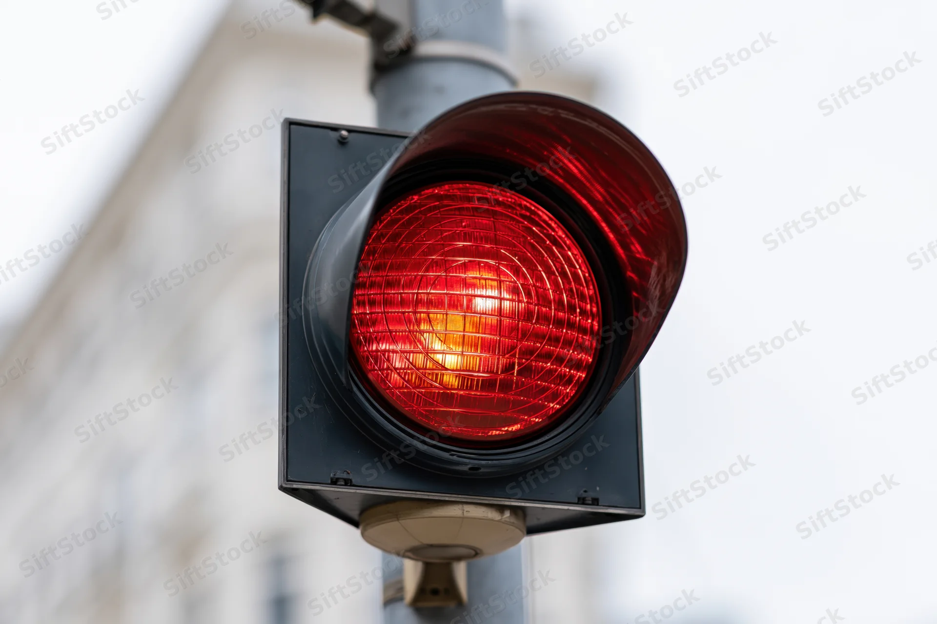Glowing red traffic light signal mounted on a pole in an urban setting