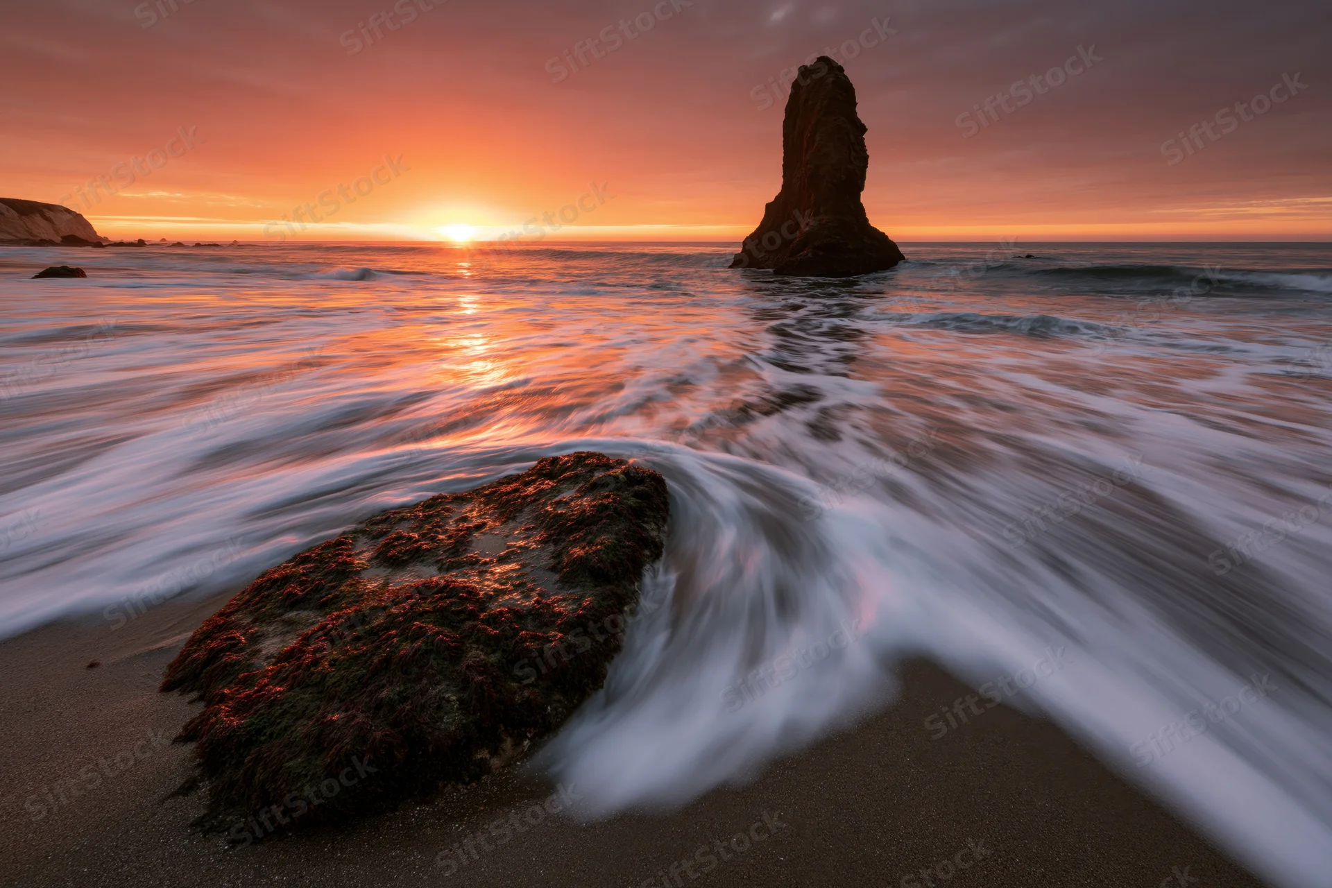 Ocean waves washing over rocks on a sandy beach at sunrise