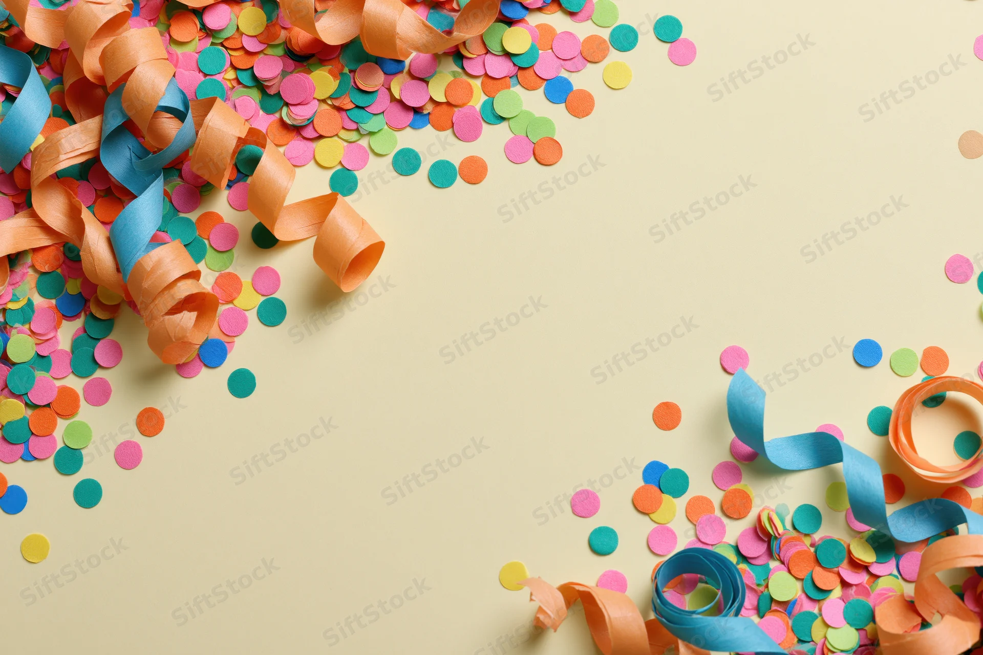 Colorful confetti dots and curled paper streamers scattered on a beige surface in a flat lay arrangement with copyspace