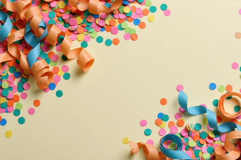 Colorful confetti dots and curled paper streamers scattered on a beige surface in a flat lay arrangement with copyspace