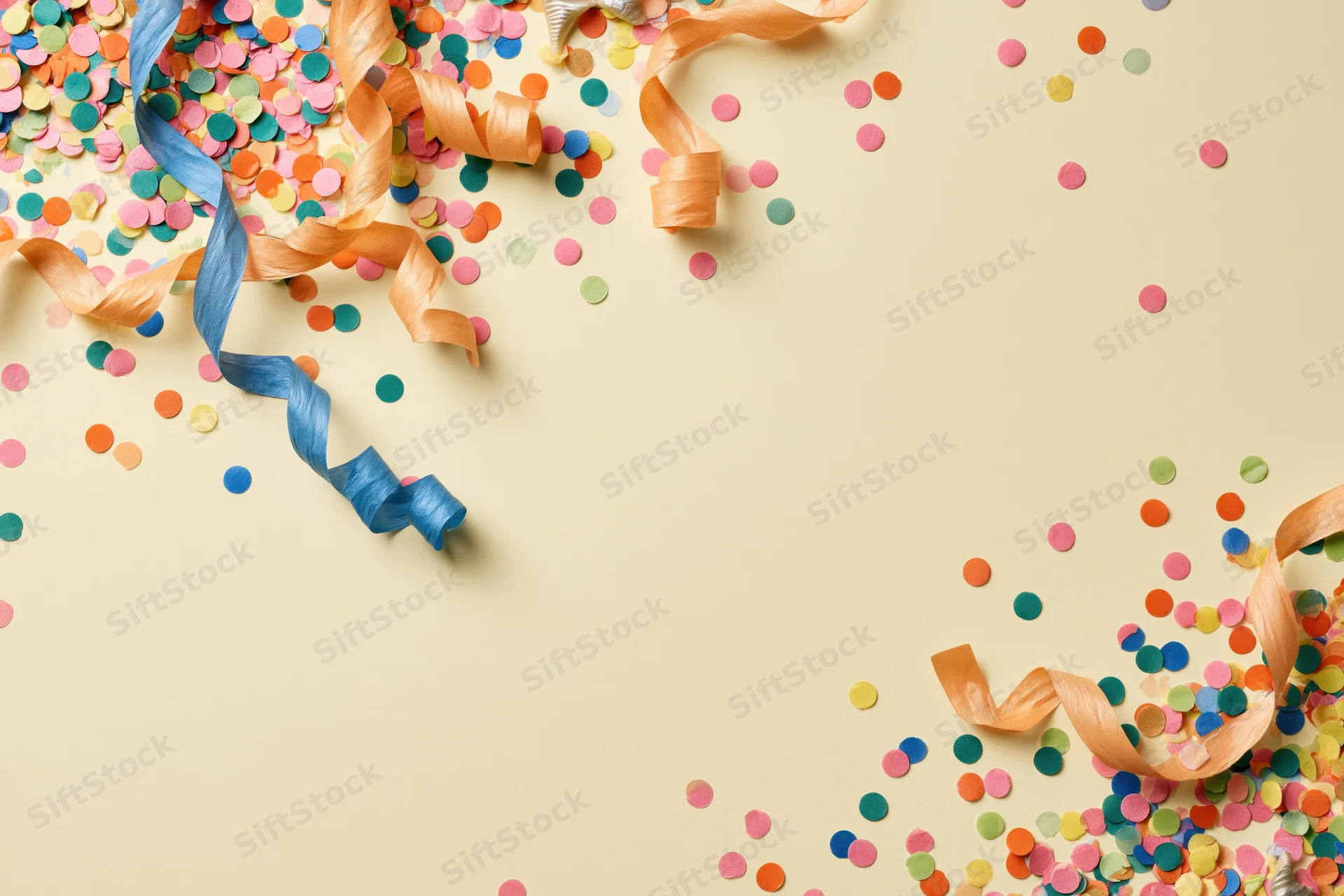 Colorful confetti and curled paper streamers scattered on beige surface with copyspace