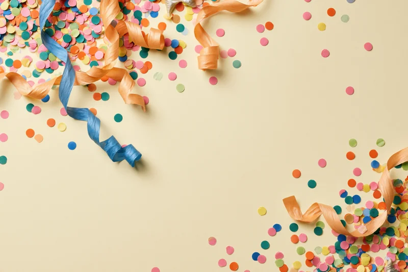 Colorful confetti and curled paper streamers scattered on beige surface with copyspace