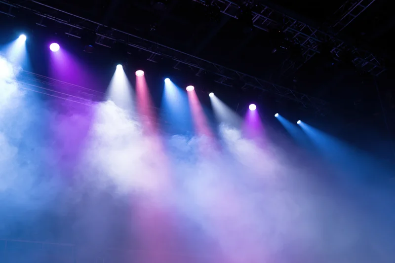 Multiple spotlights shining through smoke on a concert stage rigging viewed from below