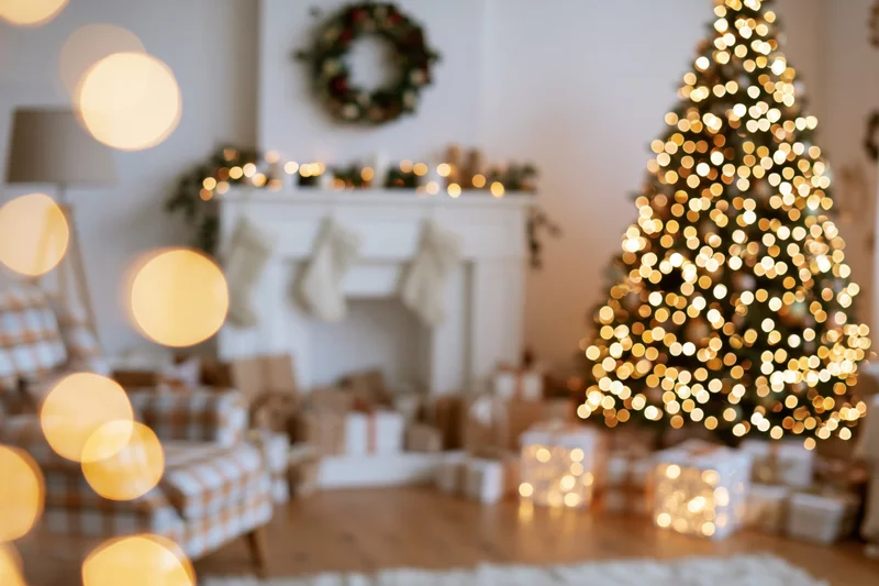 Christmas tree with lights and gifts in a cozy living room with fireplace and decorations, out of focus