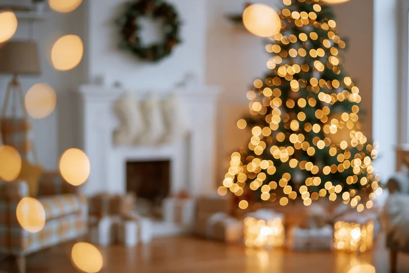 Christmas tree with glowing lights and decorations in a cozy living room with fireplace and gifts, out of focus