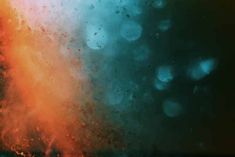 Damaged 35mm film frame showing light leaks and lens flare with orange and blue color bleed across the surface