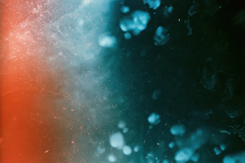 Damaged 35mm film frame showing light leaks and lens flare with red and blue color gradients and bokeh effects