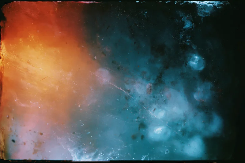 Damaged 35mm film frame showing heavy light leaks and lens flare with orange and blue color gradients