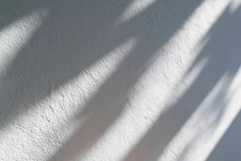 Dappled light and diagonal shadows cast across a wall