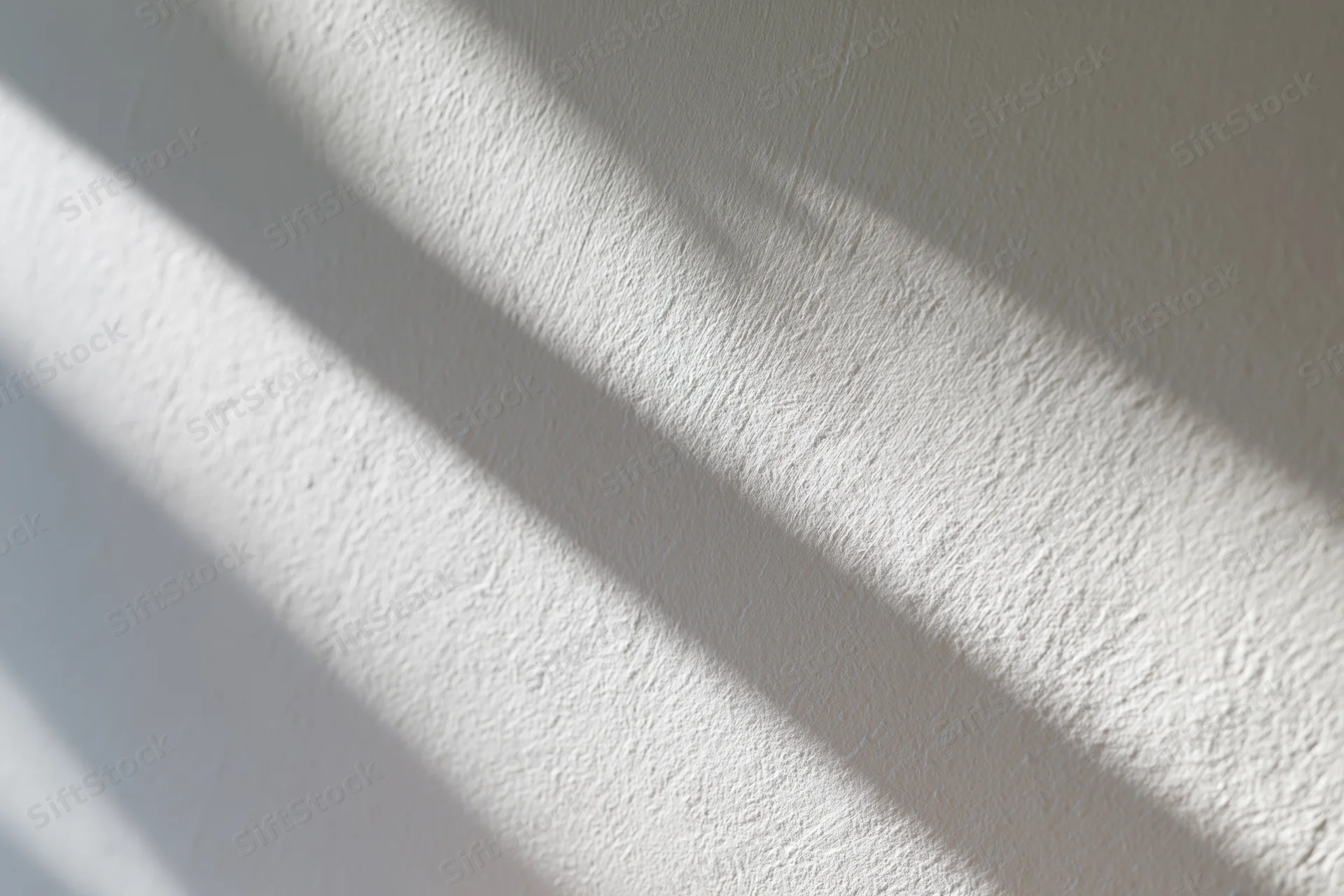 Diagonal shadows from natural light cast across a white textured wall in an interior space