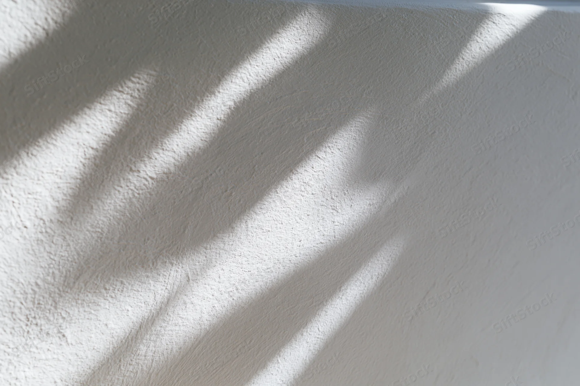 Diagonal shadows from natural light cast across a textured white wall interior