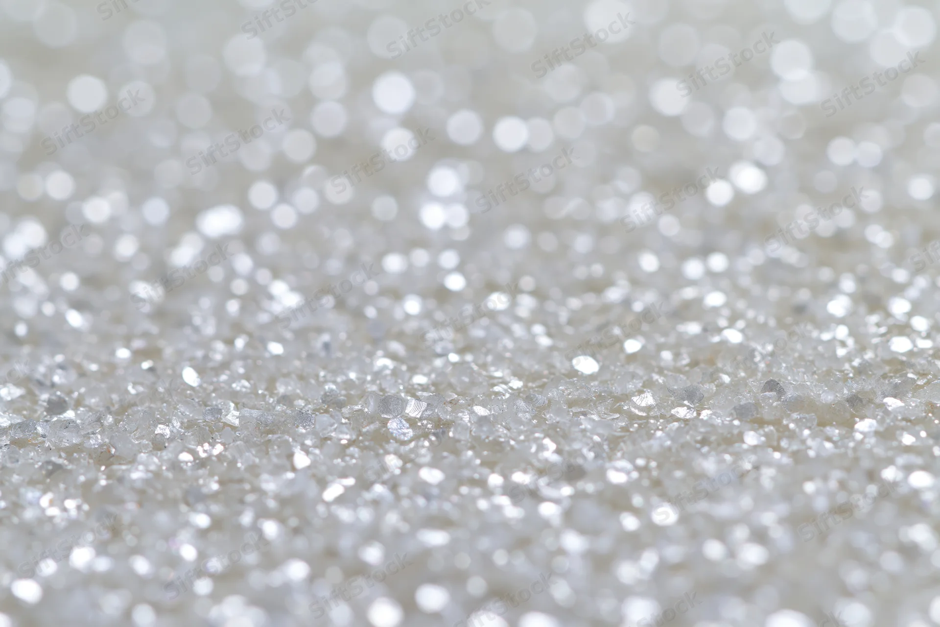 Defocused white and silver light orbs scattered across a sparkling surface as a background
