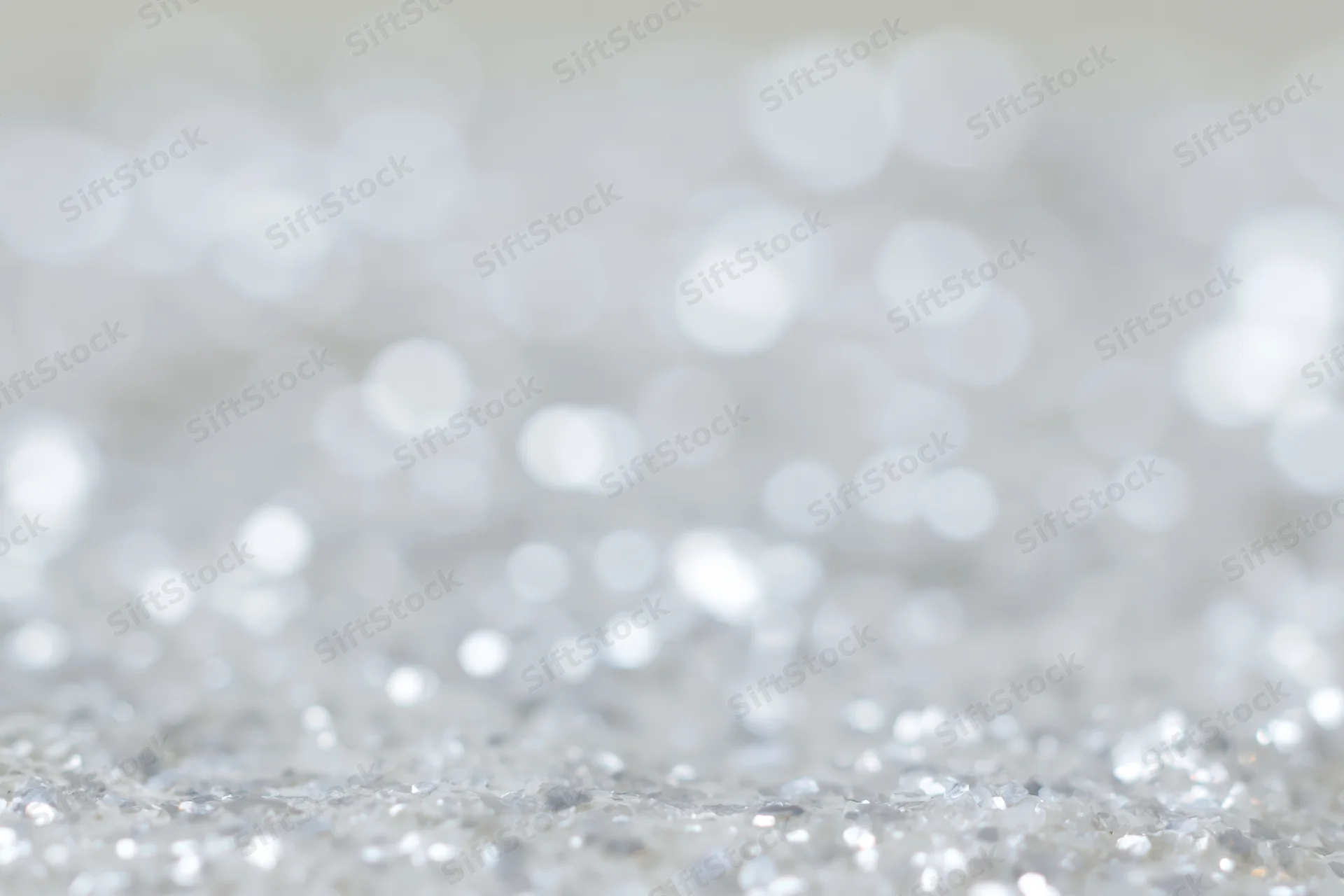 Defocused silver and white light orbs scattered across a sparkling surface as a festive background