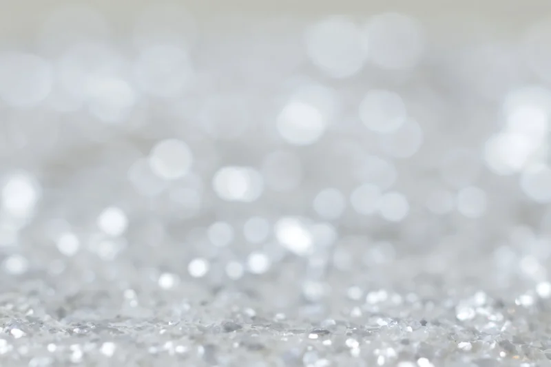 Defocused silver and white light orbs scattered across a sparkling surface as a festive background