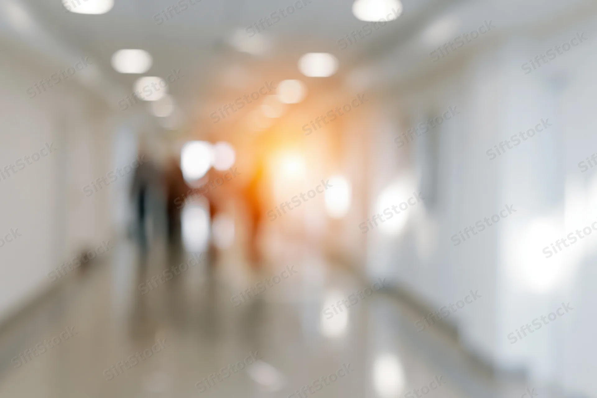Defocused view of a long white hallway with circular ceiling lights and warm glow at the end