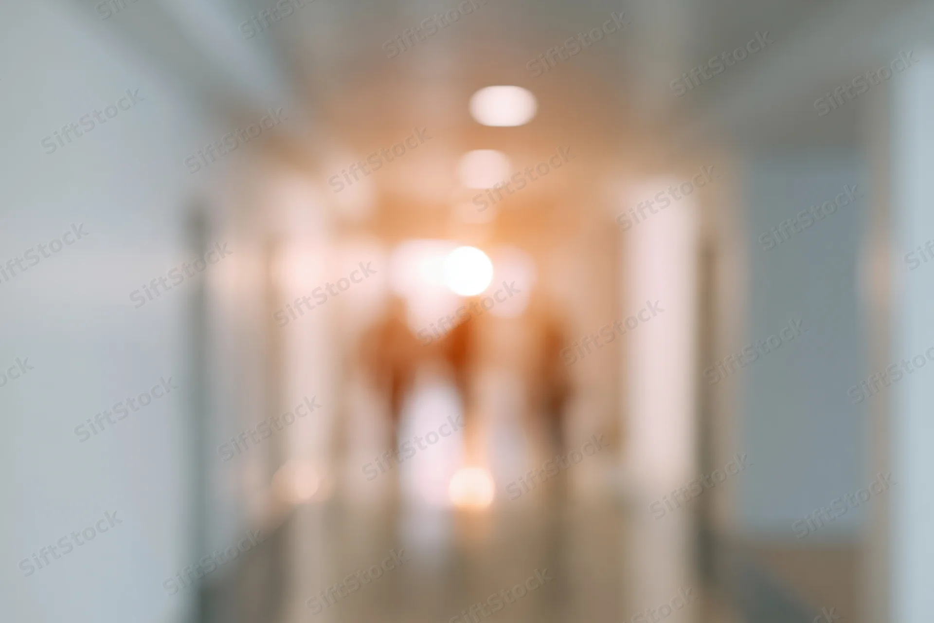 Defocused view of an empty hospital or office hallway with warm ceiling lights and tiled floor