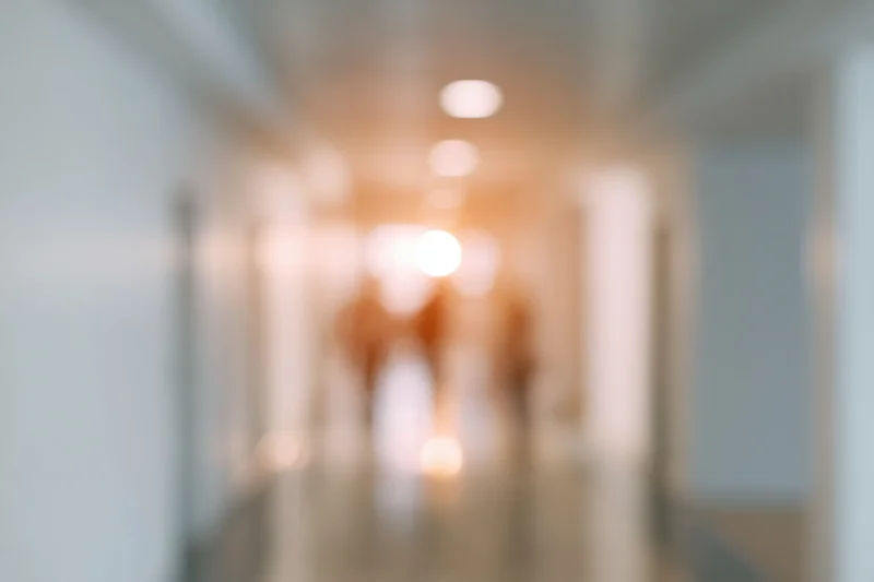 Defocused view of an empty hospital or office hallway with warm ceiling lights and tiled floor