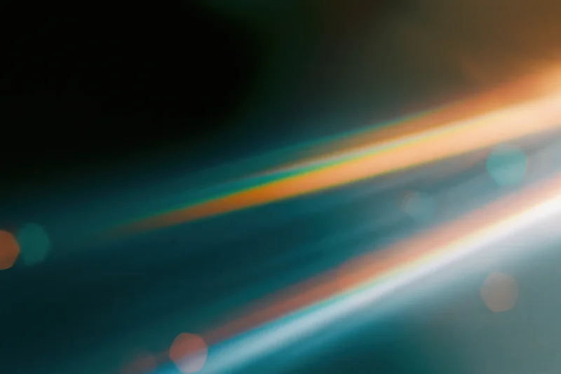 Defocused lens flare with colorful light streaks and bokeh against a dark gradient background