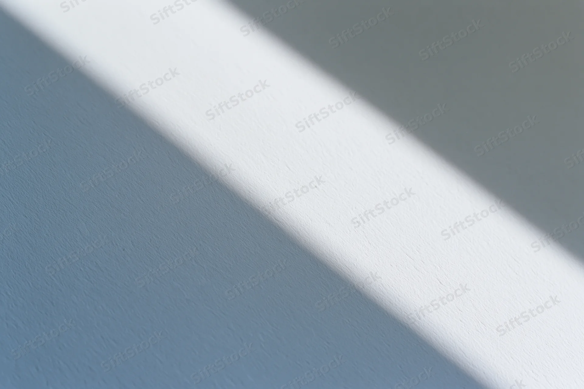 Diagonal band of natural window light across a plain blue-gray wall