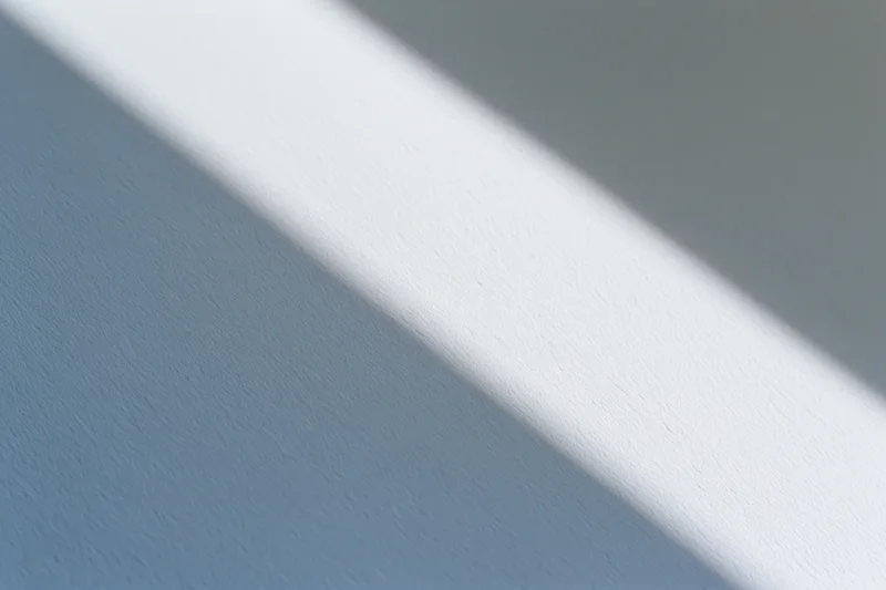 Diagonal band of natural window light across a plain blue-gray wall