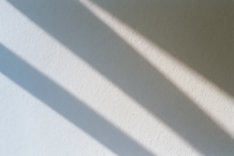 Diagonal bands of natural window light across a textured white wall interior
