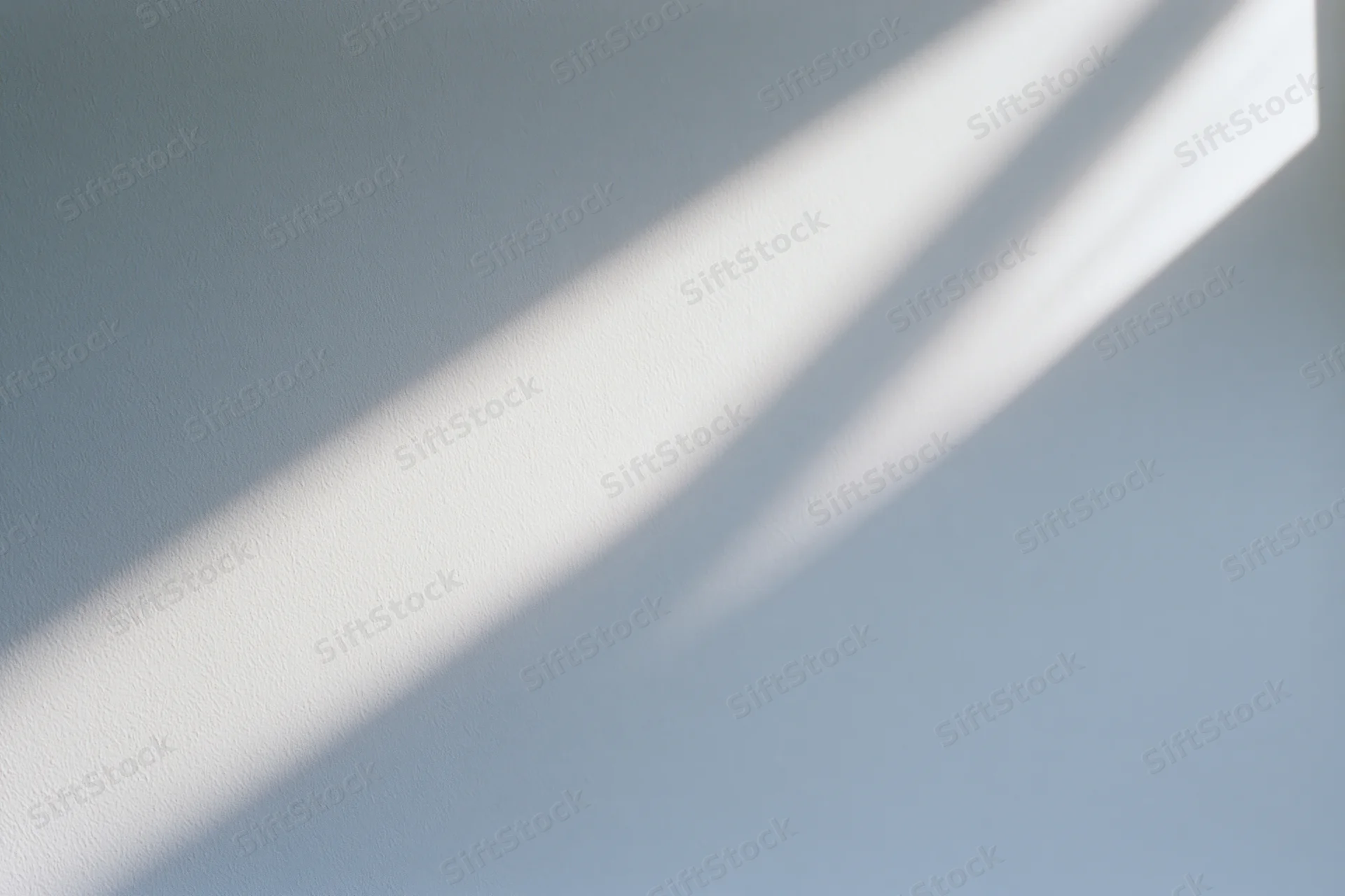 Diagonal band of natural sunlight falling across a plain interior wall