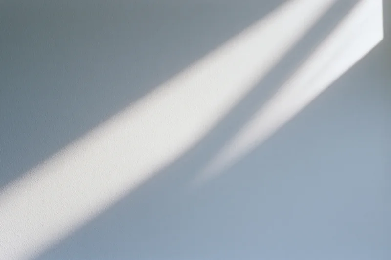 Diagonal band of natural sunlight falling across a plain interior wall