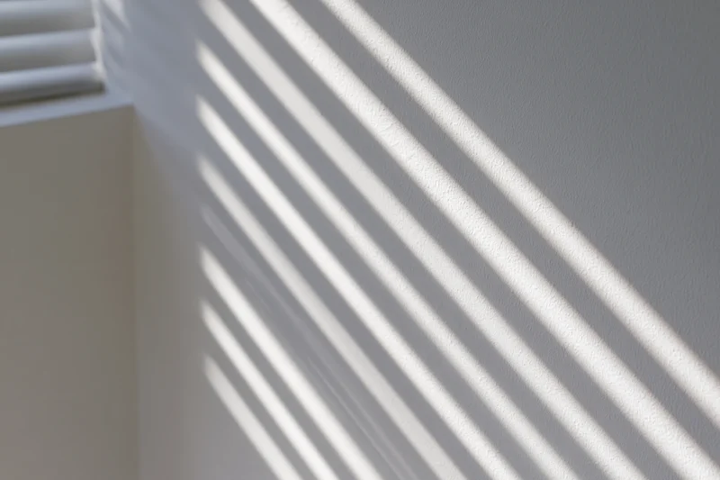 Diagonal shadows from window blinds cast across a white interior wall