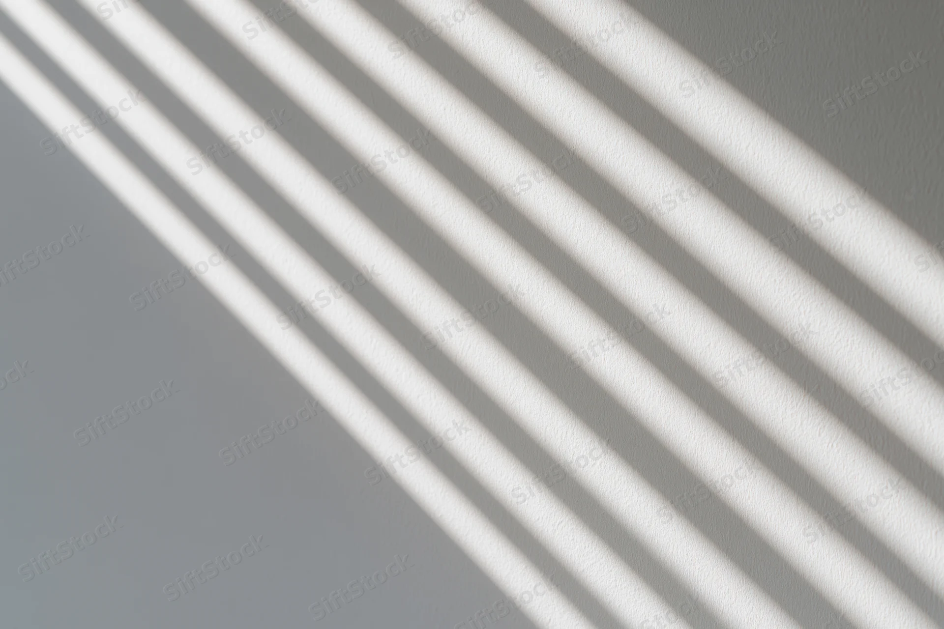 Diagonal shadows from window blinds cast across a white wall interior