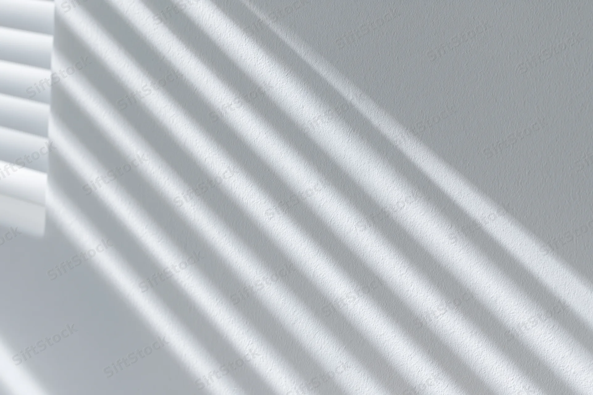 Diagonal shadows from window blinds cast across a white wall interior