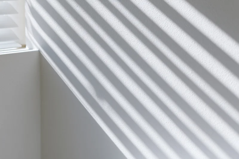Diagonal shadows from window blinds cast across a white interior wall