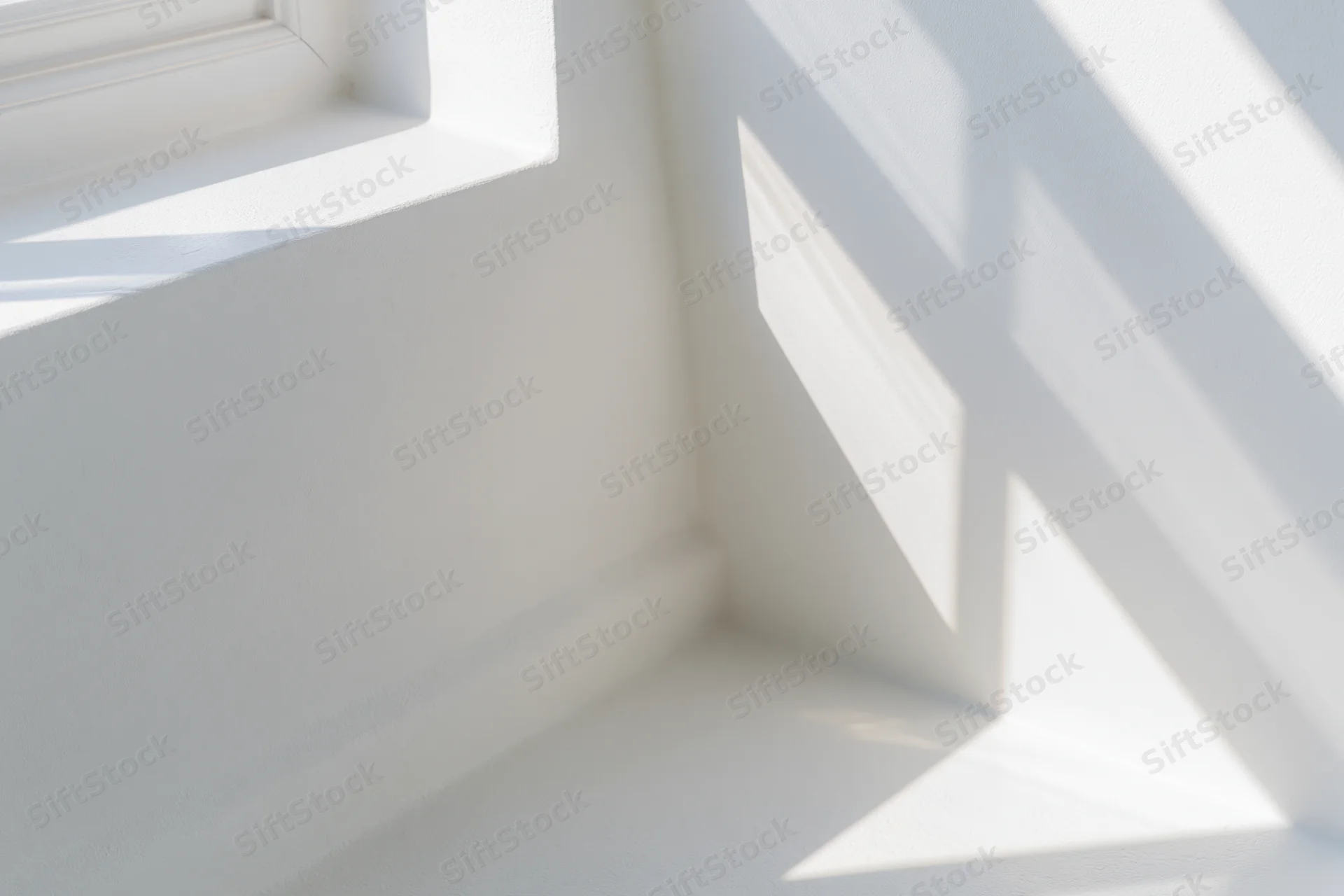 Diagonal shadows from a window frame cast across white interior walls and floor