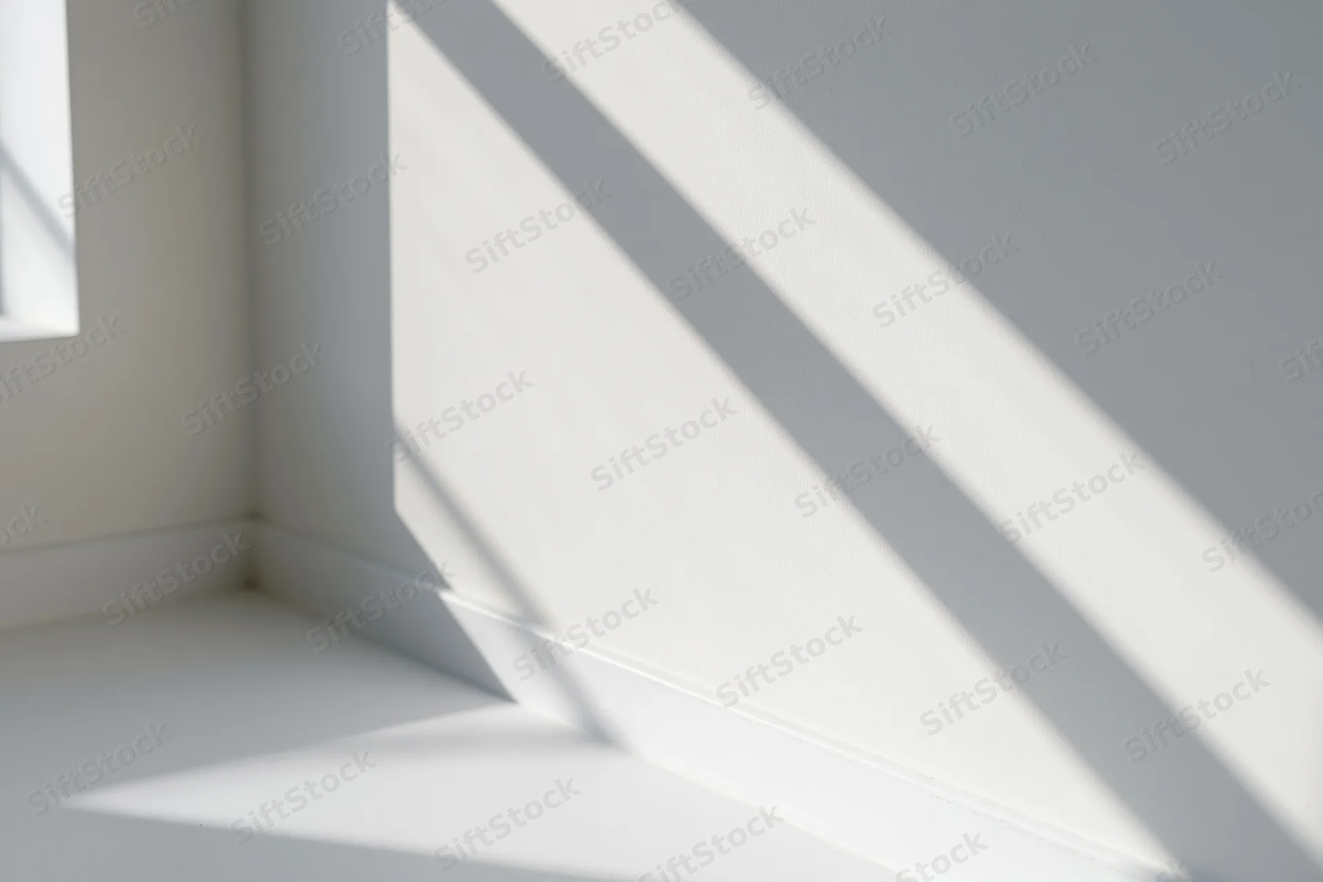Diagonal shadows from a window cast across a white interior corner, creating a pattern of light and dark on walls and floor