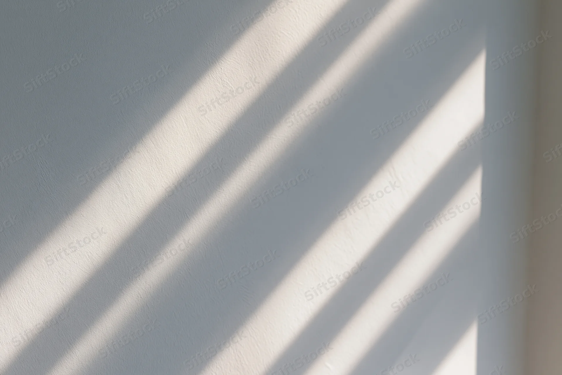 Diagonal stripes of sunlight and shadow cast across a white interior wall
