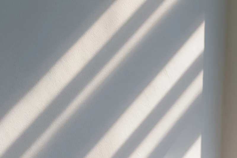 Diagonal stripes of sunlight and shadow cast across a white interior wall