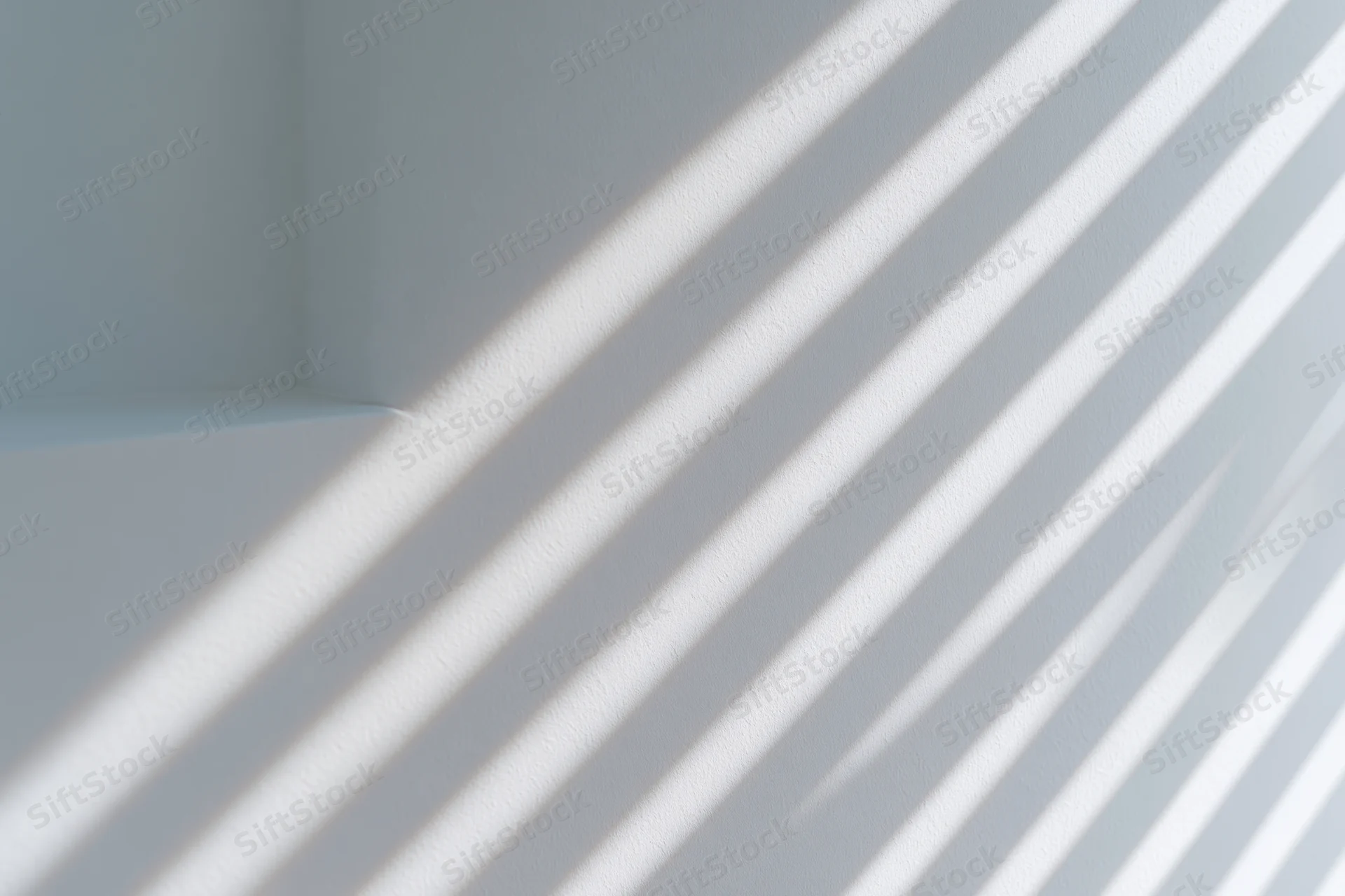 Diagonal light and shadow stripes cast across a plain white interior wall corner