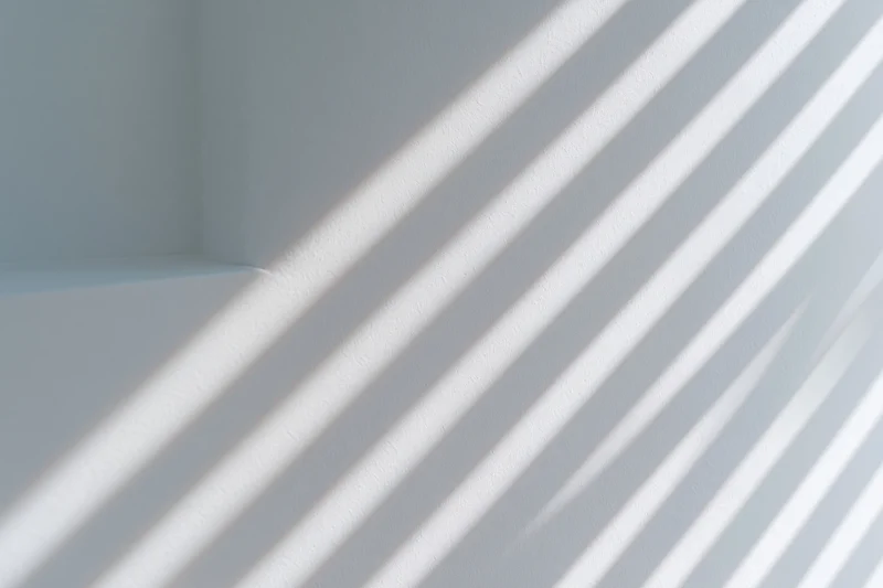 Diagonal light and shadow stripes cast across a plain white interior wall corner