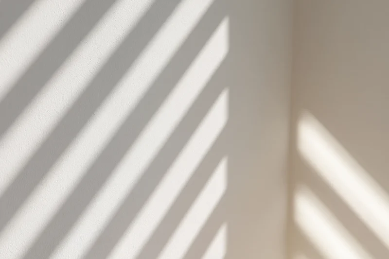 Diagonal stripes of light and shadow cast across a plain interior wall by a window