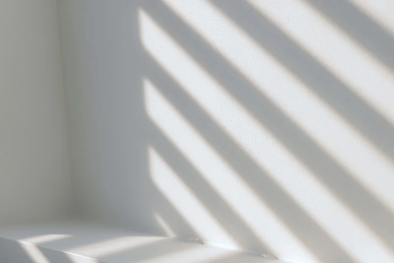 Diagonal light and shadow stripes cast across a white interior wall corner