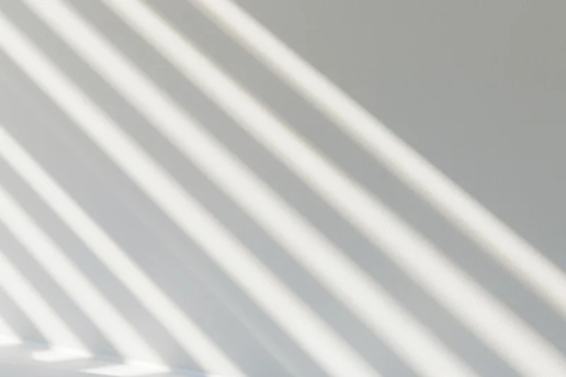 Diagonal stripes of sunlight and shadow cast across a white interior wall