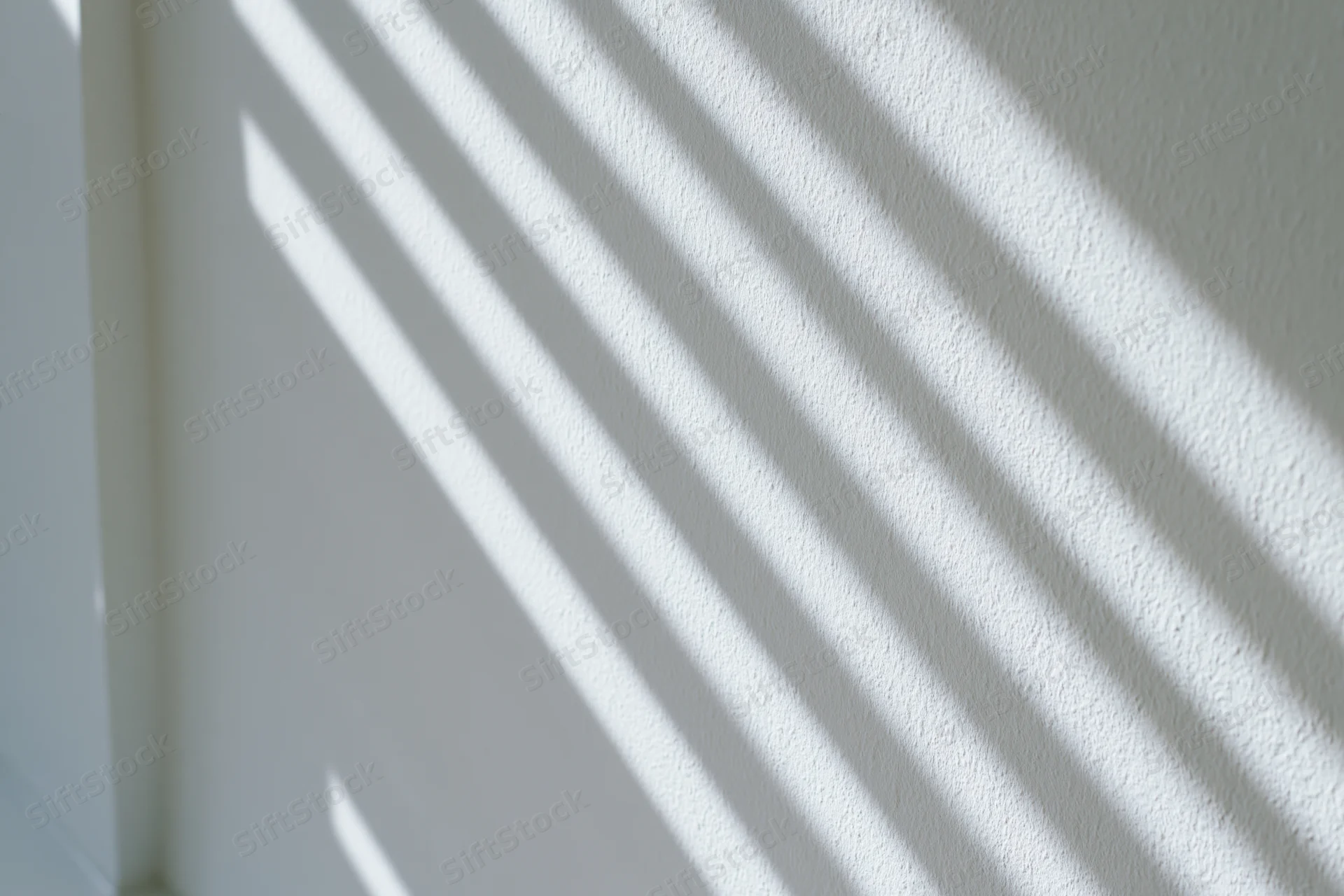 Diagonal light and shadow stripes cast across a white textured wall in an interior space