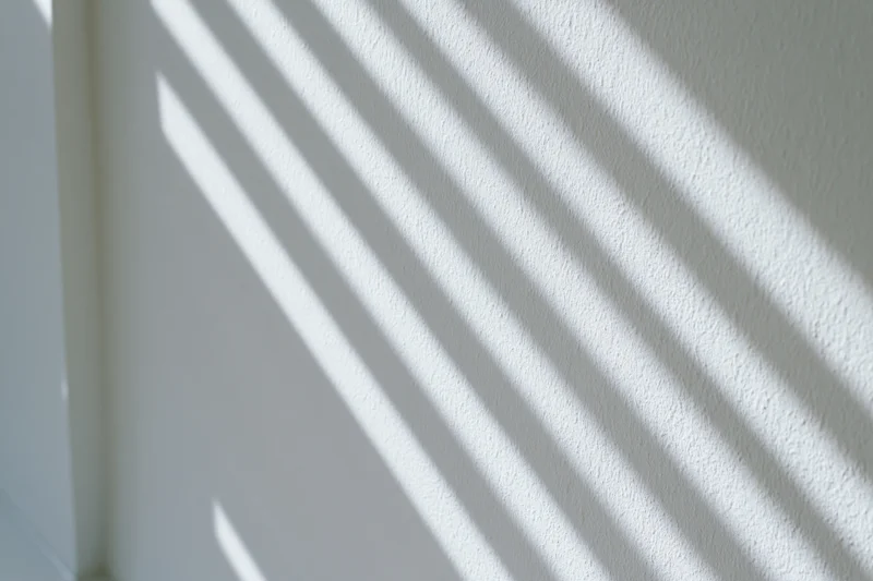 Diagonal light and shadow stripes cast across a white textured wall in an interior space
