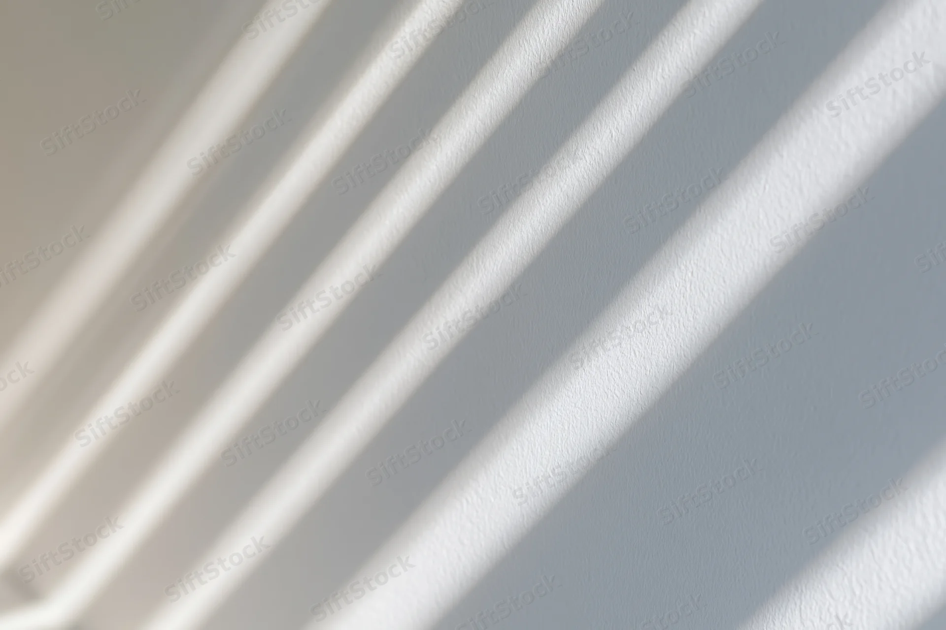 Diagonal light and shadow stripes cast across a plain white wall indoors