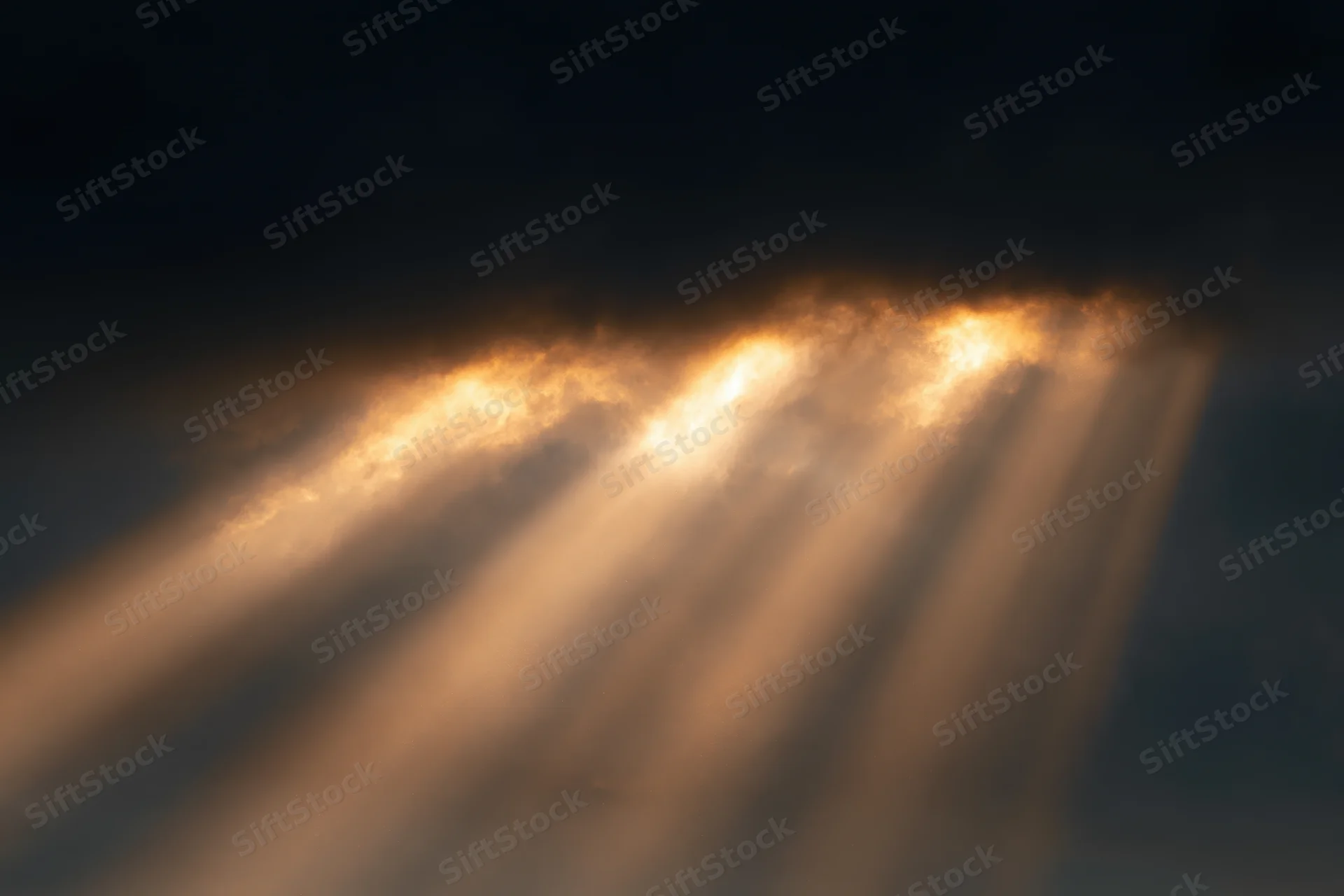 Golden sunlight beams breaking through dark clouds in the sky