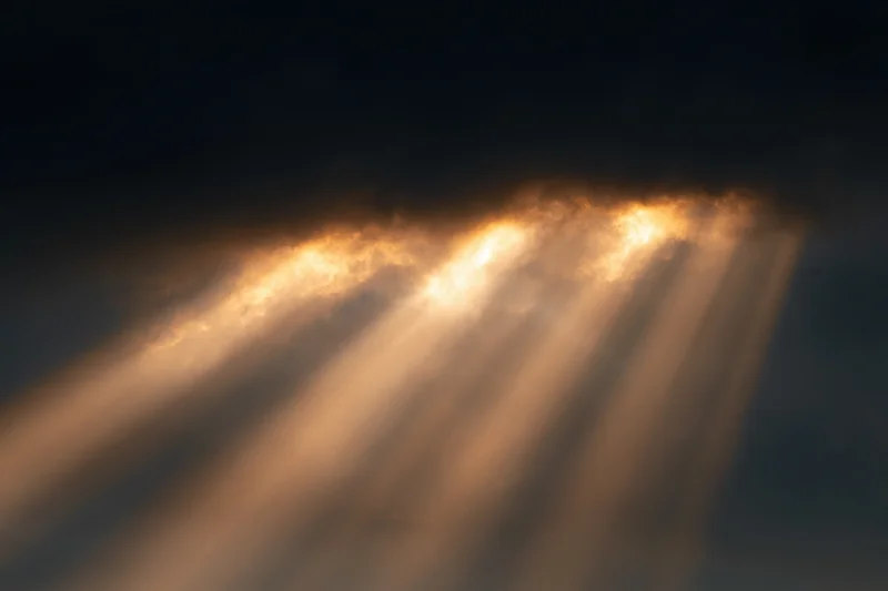 Golden sunlight beams breaking through dark clouds in the sky