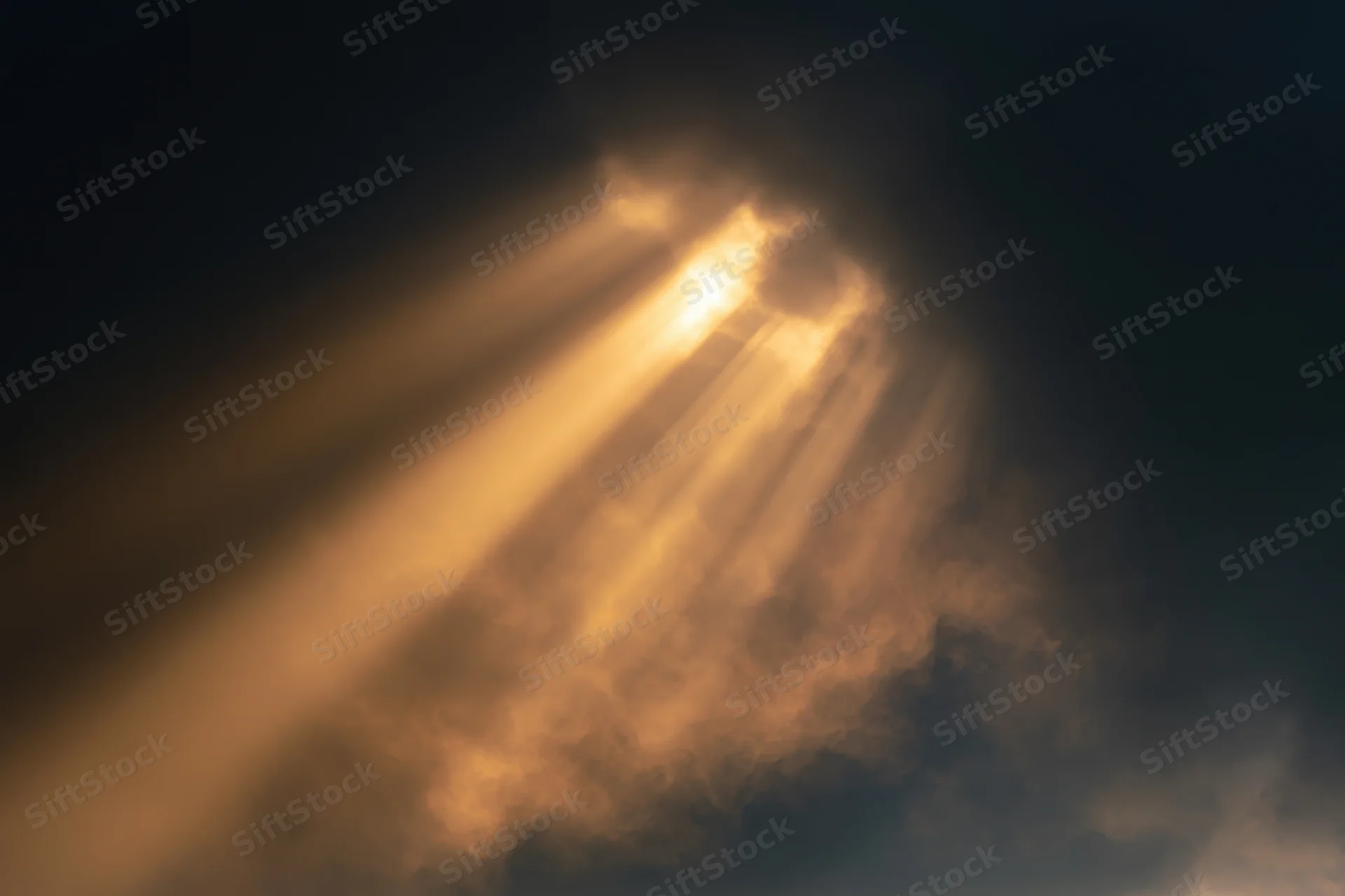 Golden sunlight beams breaking through dark clouds in the sky