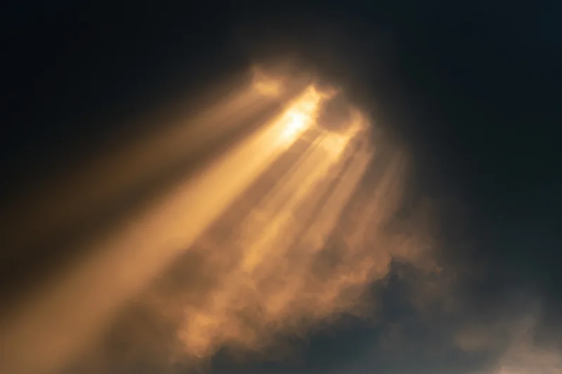 Golden sunlight beams breaking through dark clouds in the sky